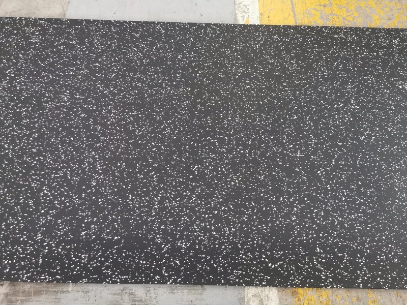 Un ingénieur inspecte de près un échantillon de revêtement de sol en caoutchouc pour y déceler des défauts.